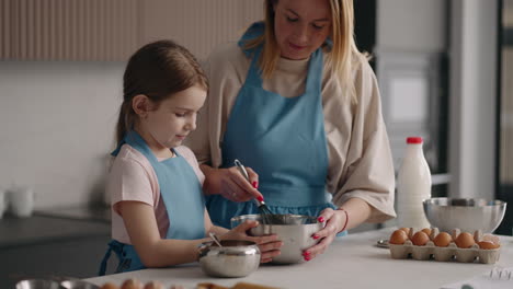 cheerful-mother-and-daughter-are-cooking-in-home-kitchen-woman-is-teaching-little-girl-to-cook-cake